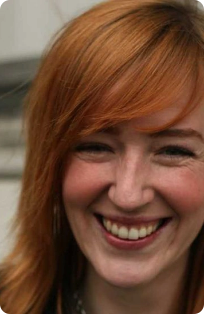 A woman with long red hair smiles warmly at the camera. She has fair skin, visible freckles, and is pictured in close-up, with a blurred background—capturing the creative spirit of About Kilkenny Animated Festival.