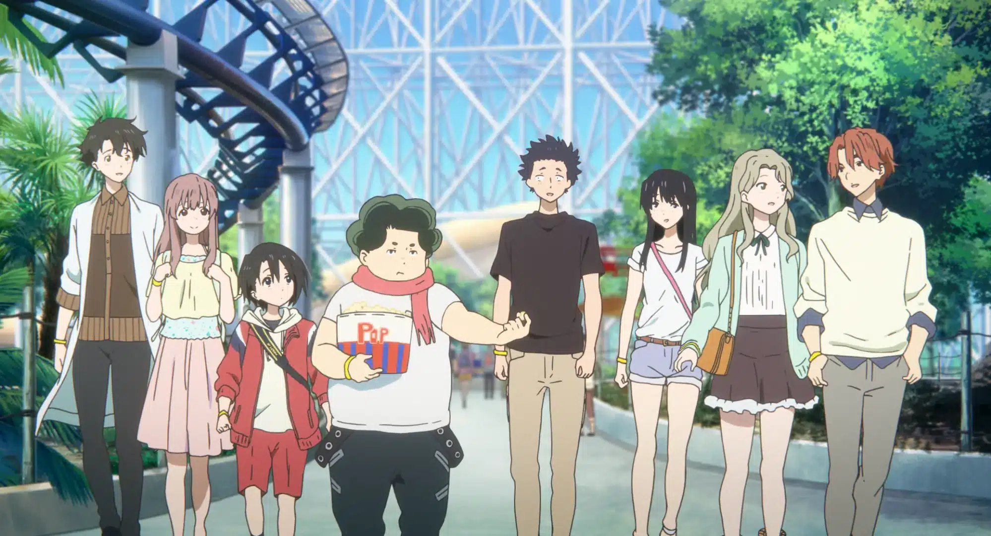 Eight animated teenagers walk together at an amusement park, with roller coaster tracks, greenery, and a glass dome structure visible in the background. One boy holds a popcorn bucket whilst others chat and smile.