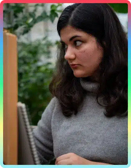 A woman with long dark hair, wearing a grey jumper, looks to the side while drawing or painting on a canvas in a green, indoor setting—capturing the creative spirit often seen at the Kilkenny Animated Festival.