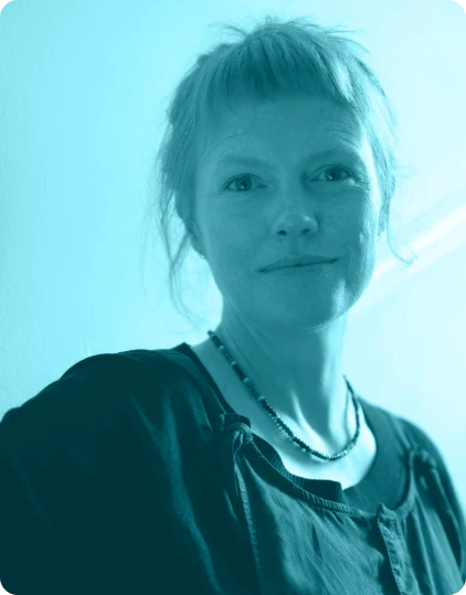 A person with short, fair hair and a necklace is looking at the camera, smiling slightly. The photo has a blue tint and soft lighting, capturing the lively atmosphere of the Kilkenny Animated Festival.