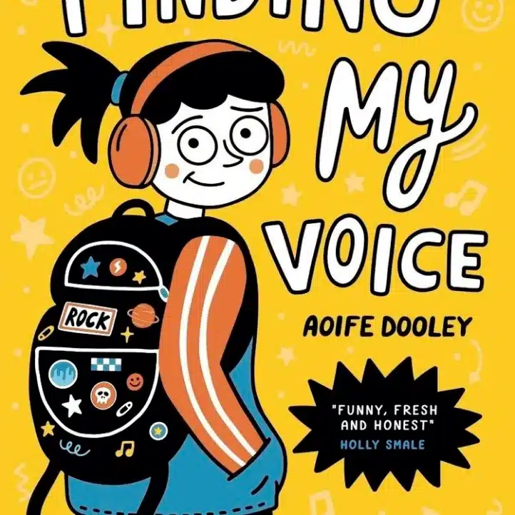 Illustrated book cover of "Finding My Voice" by Aoife Dooley. A girl with headphones and a rucksack is smiling. The background is yellow with doodles, stars, and musical notes. A black starburst quotation is at the bottom right.