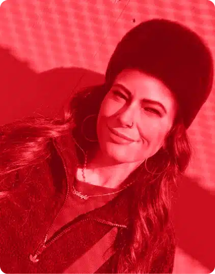 Woman with long hair in a furry hat and hoop earrings smiles outdoors at the Kilkenny Animated Festival. The image has a strong red filter and is tilted, with shadows in the background.