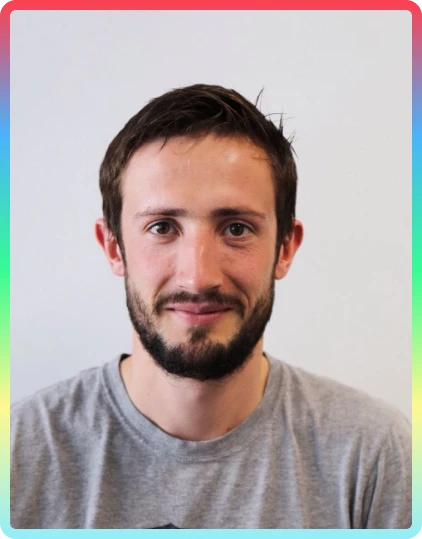 A man with short brown hair and a beard smiles slightly at the camera. He is wearing a grey T-shirt. The photo, featuring a colourful gradient border, was taken during the vibrant Kilkenny Animated Festival.