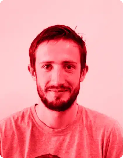 A man with short brown hair and a beard is smiling slightly, wearing a T-shirt. The image, reminiscent of creative portraits seen at Kilkenny Animated Festival, features a red colour filter and a plain background.