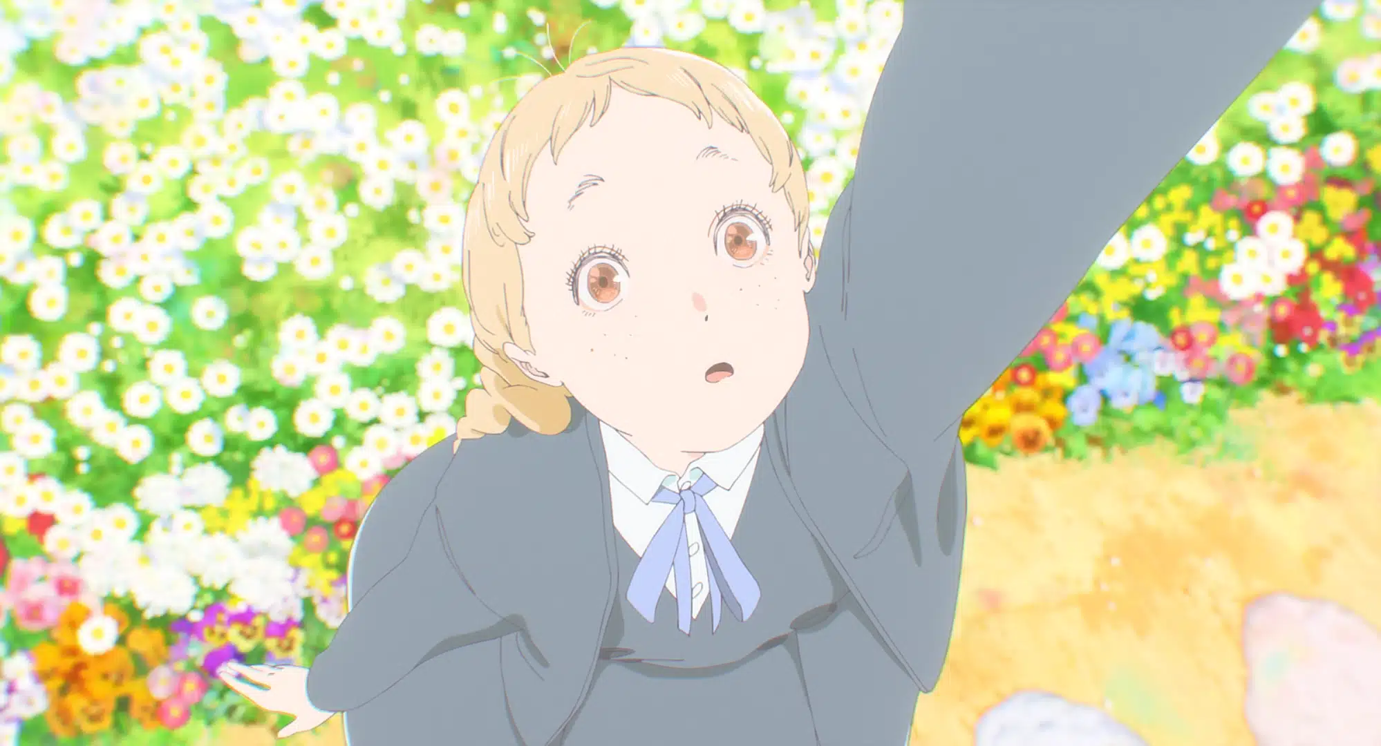 An animated girl with short blonde hair and freckles looks upwards, reaching out her arm. She stands in front of a field of white and yellow flowers, wearing a grey school uniform with a blue tie.