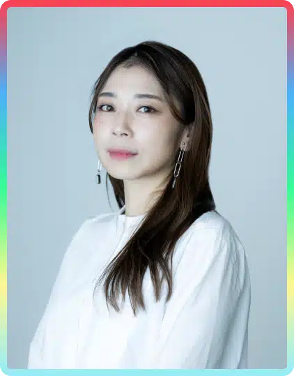 A woman with long brown hair wearing a white blouse and dangling earrings poses against a plain background with a colourful border around the image, evoking the lively spirit of the Kilkenny Animated Festival.