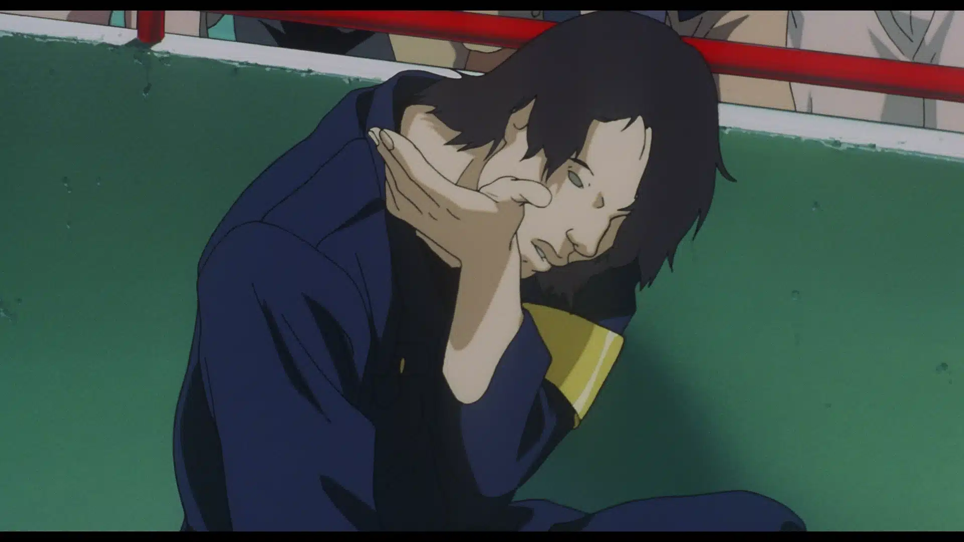 An animated person in a dark uniform sits on the ground, resting their head on their hand, looking distressed, with a green wall and red railing behind them.