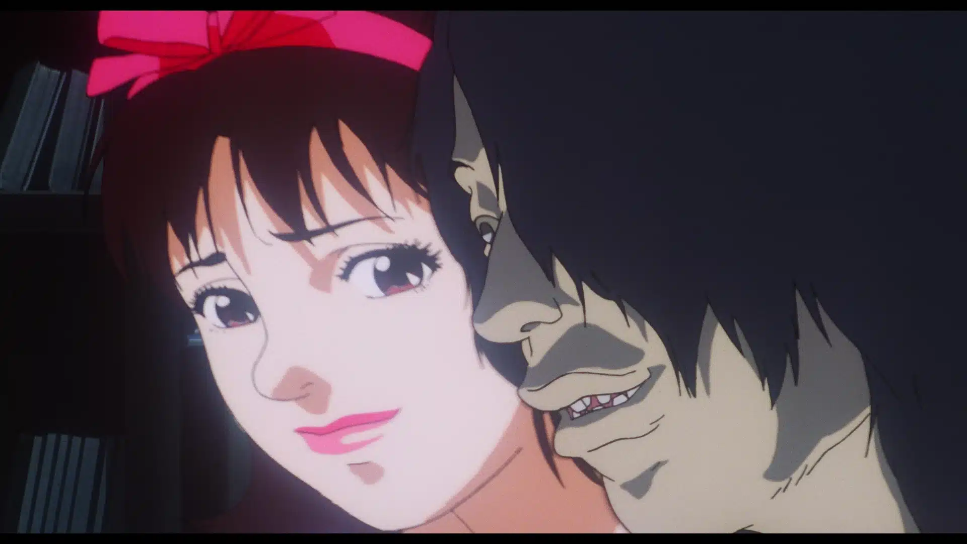 A smiling woman with a pink bow is closely approached from behind by a sinister-looking man with long dark hair, half of his face in shadow. The background is dark and blurred.