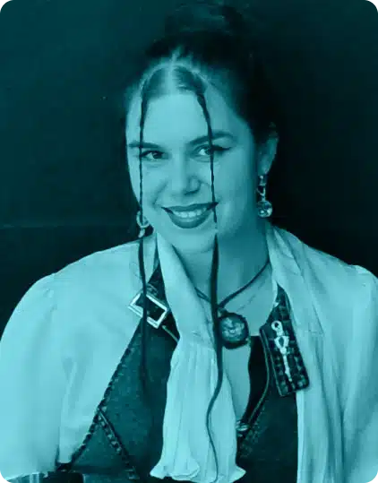A woman with long dark hair, two front strands loose, smiles at the camera. She wears layered clothing, earrings, a necklace, and a badge—all in a blue-tinted image capturing the vibrant spirit of the Kilkenny Animated Festival.