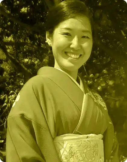 A woman wearing a traditional kimono smiles outdoors at the Kilkenny Animated Festival. The image has a yellowish tint and trees are visible in the background.