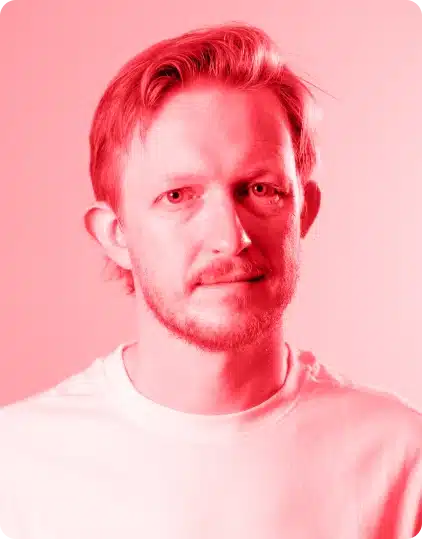 A man with short, fair hair and a beard looks at the camera. He is wearing a plain white shirt, and the image—bathed in a strong red tint—captures the vibrant energy reminiscent of the Kilkenny Animated Festival.