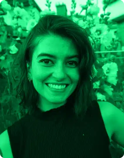 A person with shoulder-length hair smiles outdoors in front of blooming flowers during the Kilkenny Animated Festival. The image has a strong green colour filter.