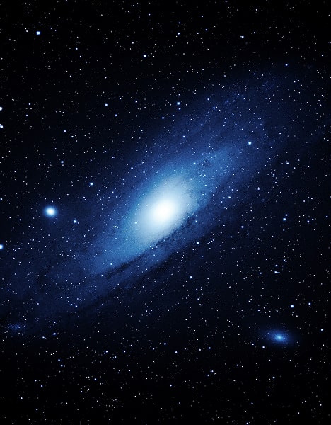 A bright spiral galaxy glows in the centre, surrounded by countless stars scattered across a dark, star-filled night sky.